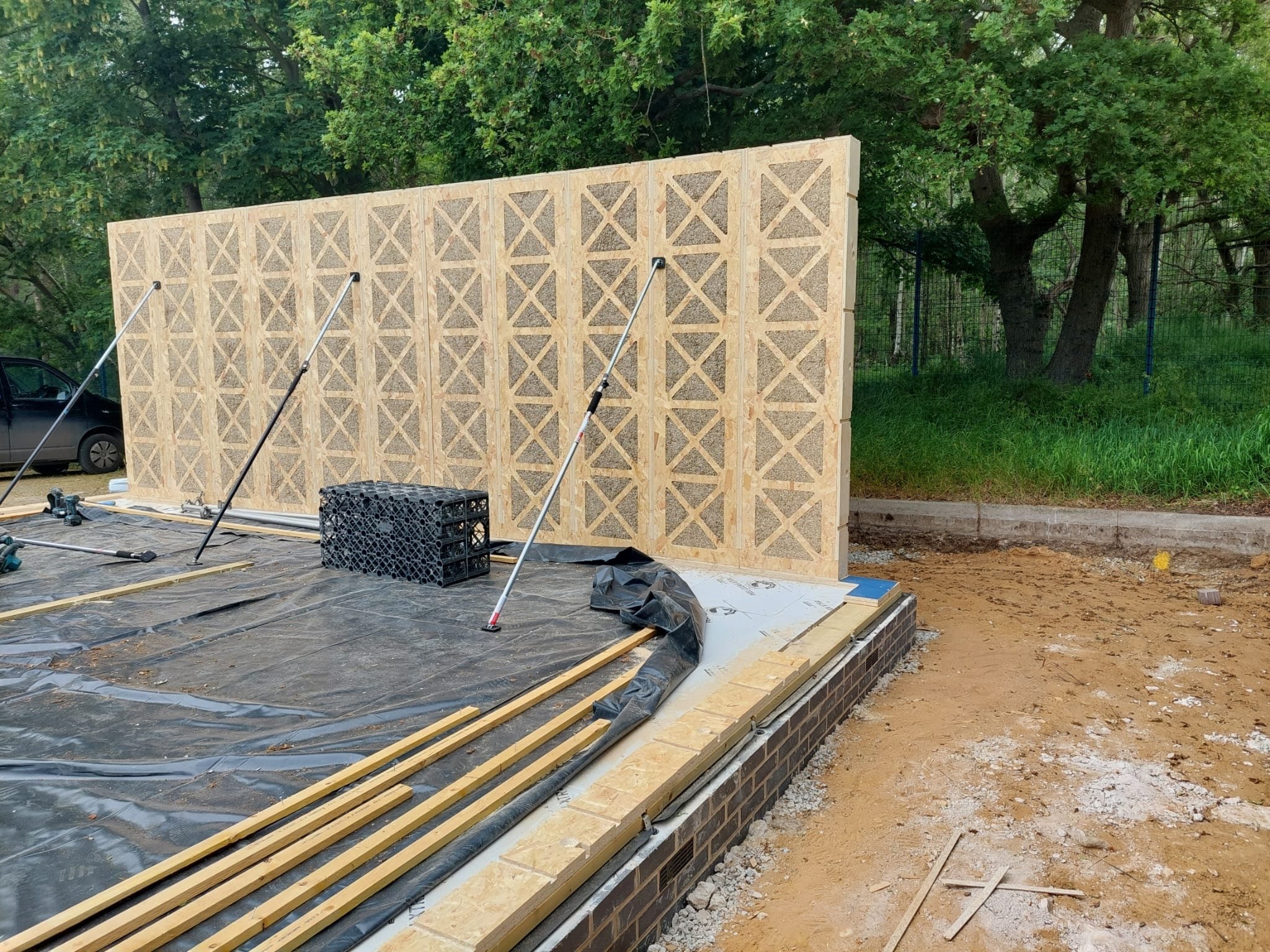 Construction site showing prefabricated hemp and plywood cassette wall panels being installed, demonstrating innovative sustainable and regenerative building techniques.